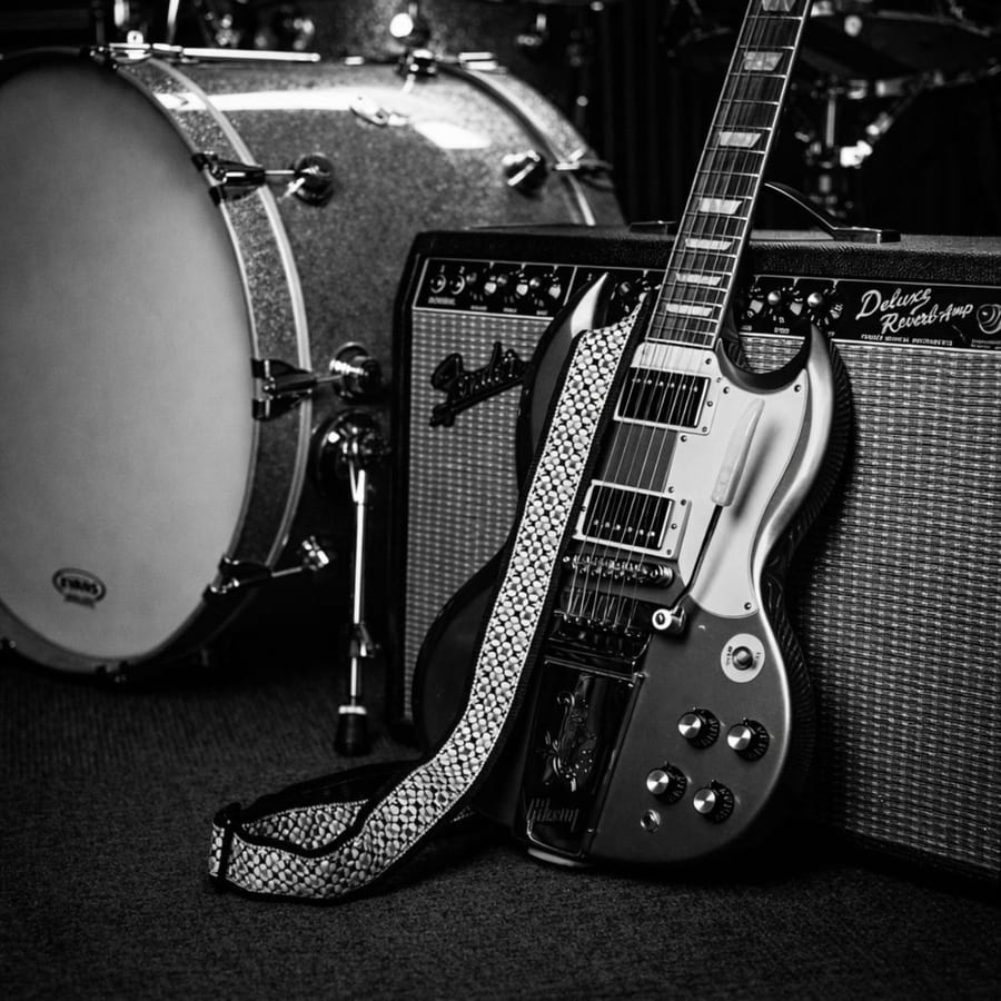 Guitarra encostada ao amplificador, bateria ao fundo — fotografia a preto e branco